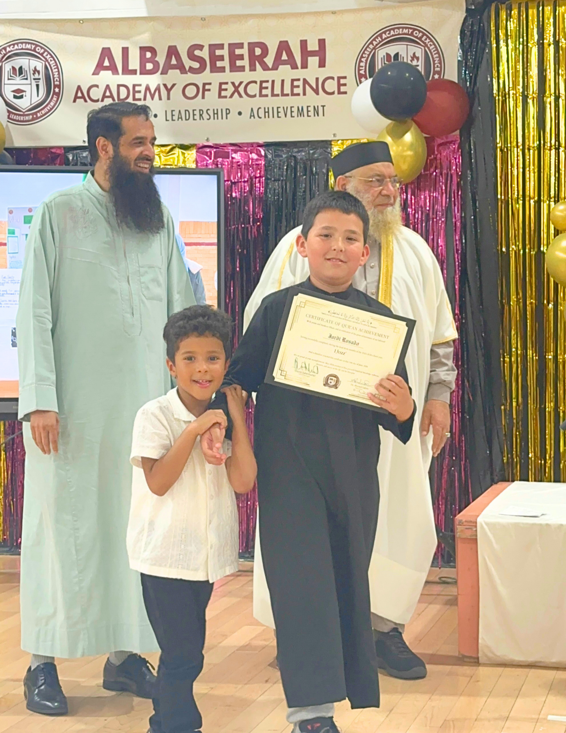A proud Albaseerah student holding his certificate with his teachers